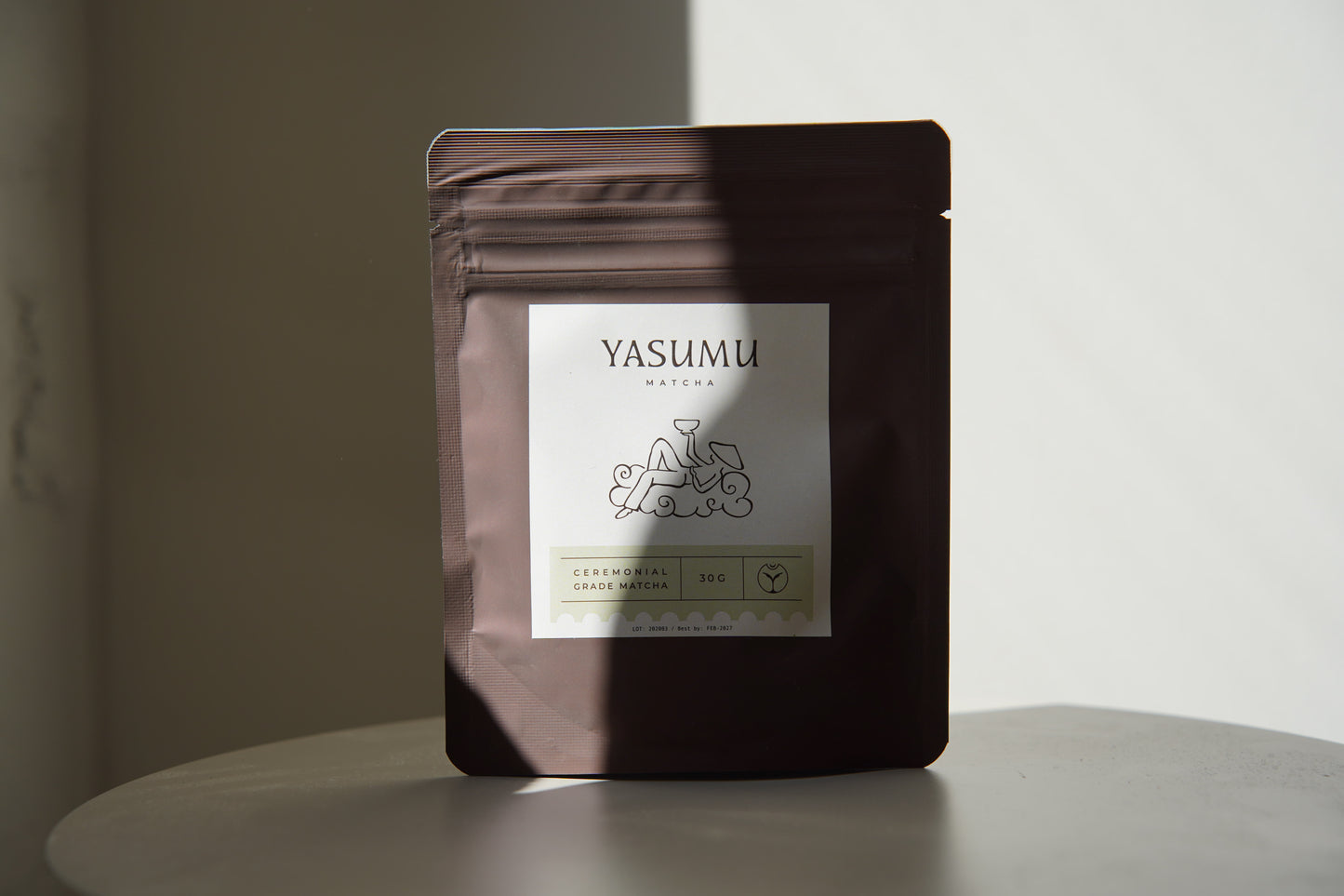Yasumu Matcha complete set with bamboo whisk, ceremonial matcha pouch, white matcha tin, and bamboo scoop box displayed on round white table in natural light