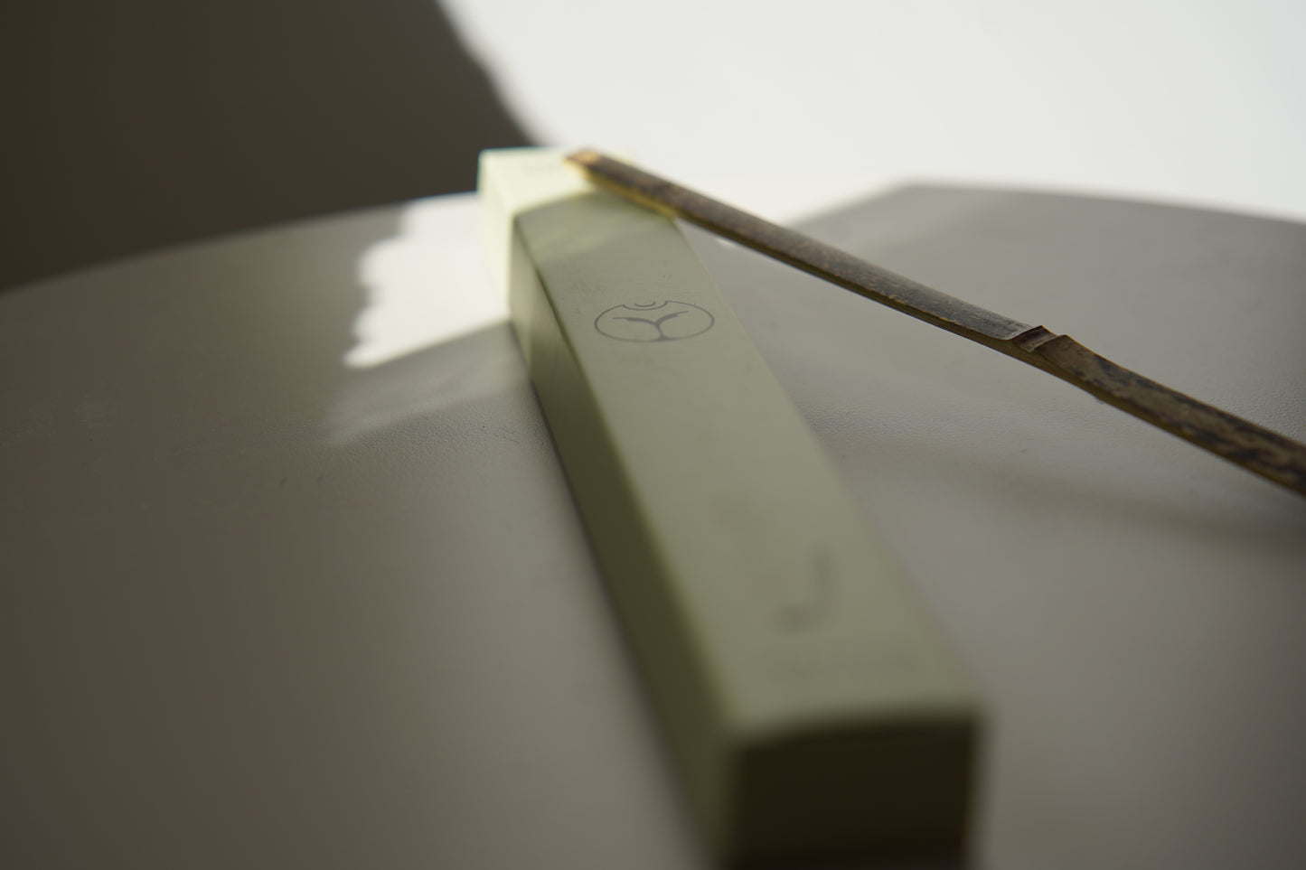 Yasumu bamboo matcha scoop resting on light green box with Yasumu logo on round white table in soft shadow
