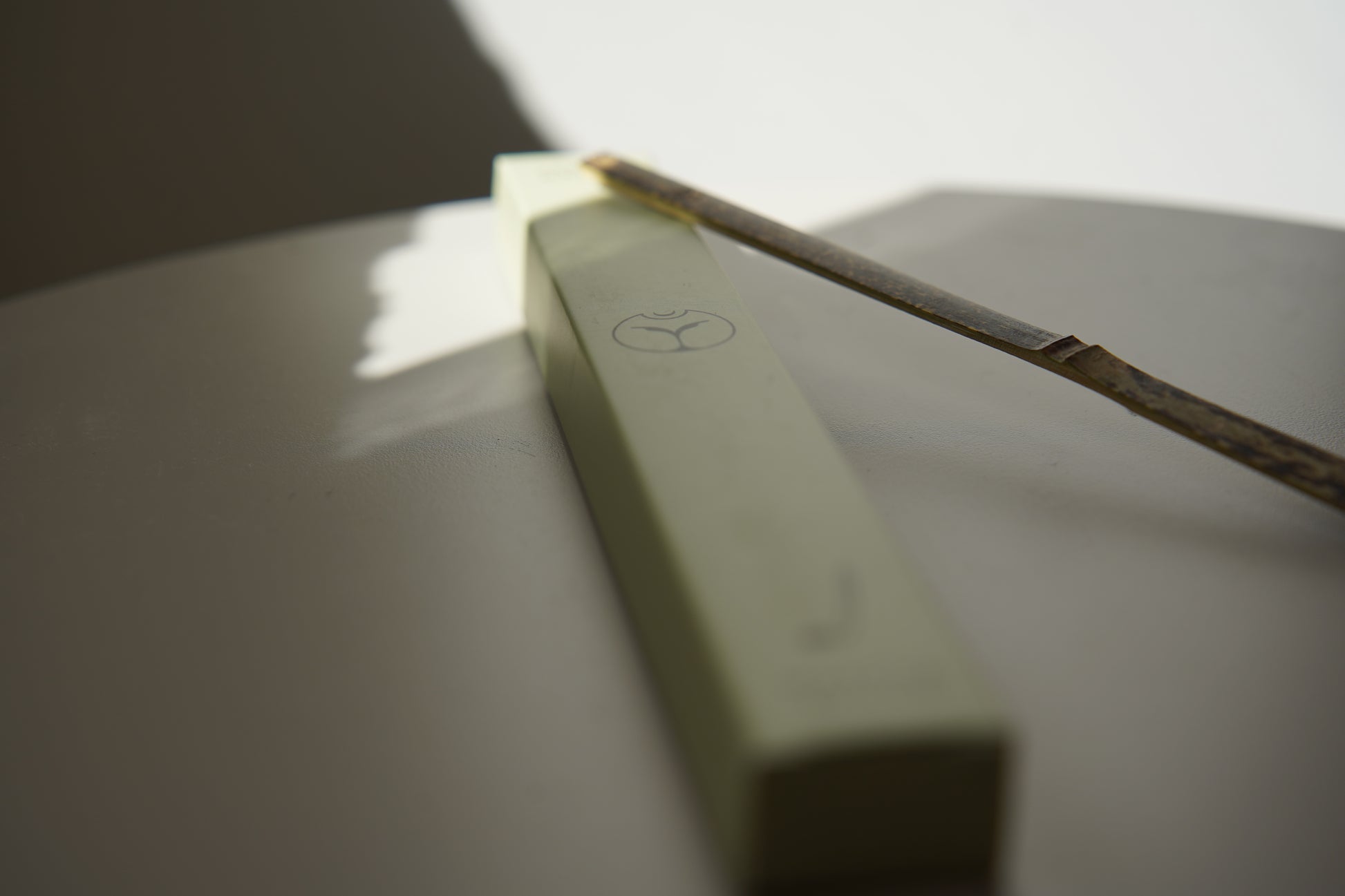 Yasumu bamboo matcha scoop resting on light green box with Yasumu logo on round white table in soft shadow